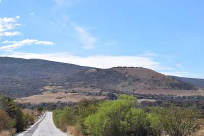 Scenic view of road leading towards mountains against sky