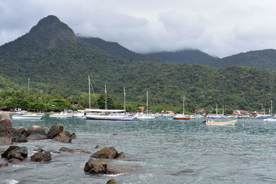 Sailboats on sea by mountains against sky