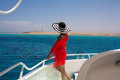 A girl in a black and white striped beach hat, bikini and coral beach poreo travels on a yacht. 