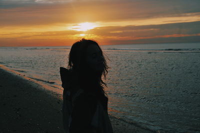 Silhouette woman standing on beach against sky during sunset