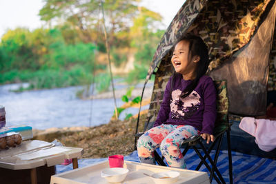 Girl laughing while sitting on chair against tent