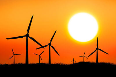 Silhouette wind turbines on field against orange sky