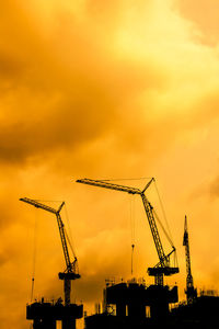 Low angle view of silhouette cranes against sky during sunset