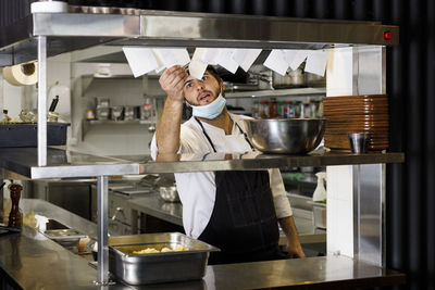 Chef with protective face mask checking ticket holder in restaurant