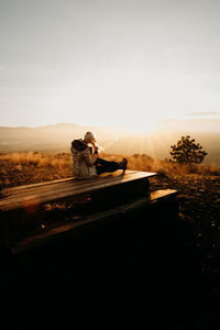 Rear view of woman sitting on field against sky during sunset