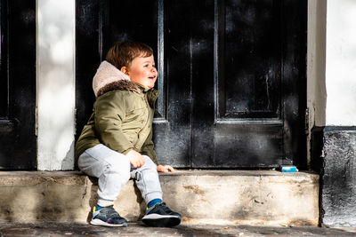 Smiling boy sitting by closed house door