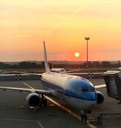 Airplane at airport runway against sky during sunset