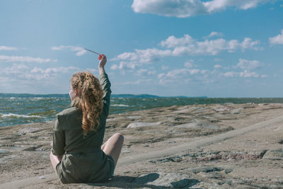 Man sitting at beach against sky