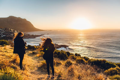 Rear view of people walking on beach against sky during sunset