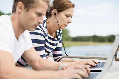 Side view of mature couple using laptops while lying on pier