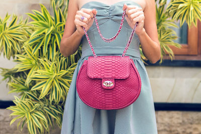 Midsection of woman holding pink while standing against wall