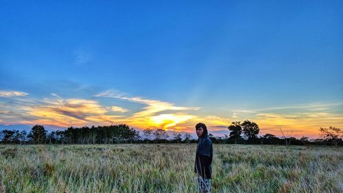 Woman standing on field against sky during sunset