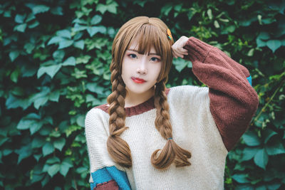 Portrait of young woman with braided hair standing against plants at park