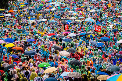 Crowd of people wearing multi colored raincoat and umbrella outdoors