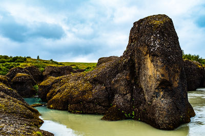 Rock formation by river against sky