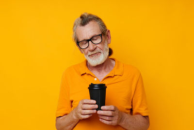 Portrait of senior woman drinking bottles against yellow background