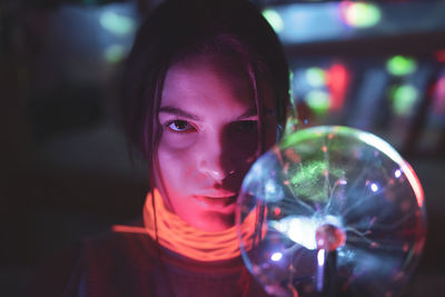Close-up portrait of woman holding illuminated lighting equipment in darkroom