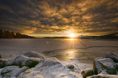 Scenic view of beach against dramatic sky during sunset