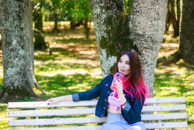 Beautiful young woman having drink while sitting on bench at park