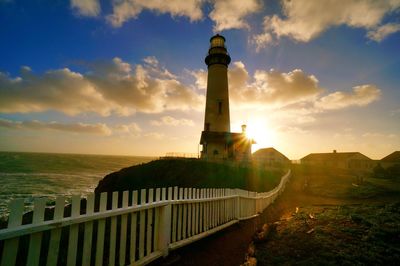 Lighthouse on beach against cloudy sky