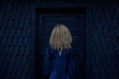 Blond woman standing in front of closed door at night