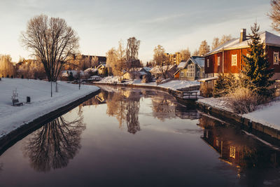 Reflection of bare trees and buildings in lake during winter