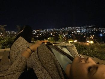 Midsection of woman lying in illuminated city against sky at night