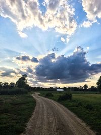 Road passing through field against cloudy sky