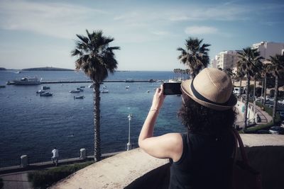 Rear view of woman photographing sea through mobile phone