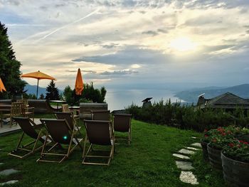 Empty chairs and table by grass against sky