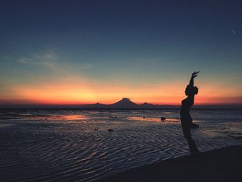 Silhouette woman standing on beach against sky during sunset