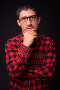 Portrait of young man standing against black background