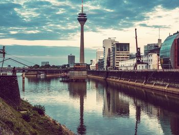Modern buildings by river against sky in city