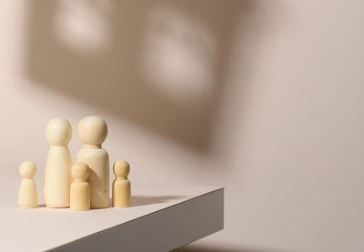 Wooden figurines of a family on a background of shadow in the form of a house. beige 