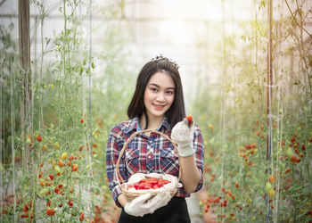 Portrait of smiling young woman holding strawberry at farm