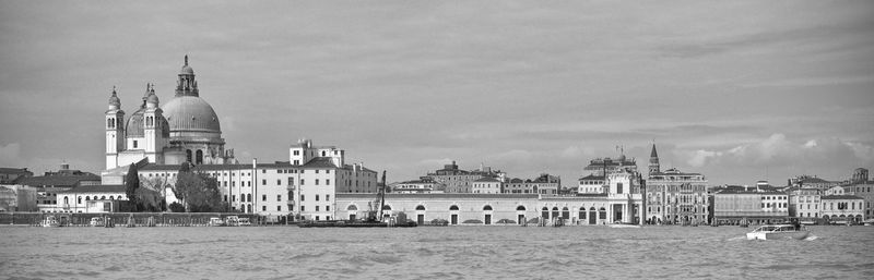 View of buildings by sea against cloudy sky