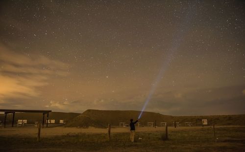 Rear view of man lighting flashlight star field in sky