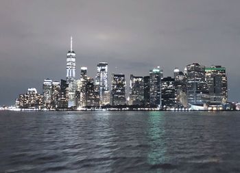 Illuminated buildings by sea against sky