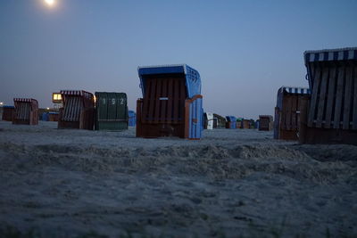 Hooded beach chairs on sand against clear sky at sunset