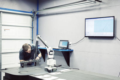 Male worker working on steel with machine by wall at industry