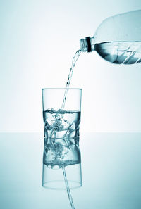 Close-up of glass pouring water against white background