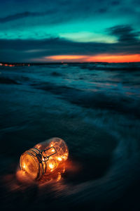 Illuminated light in sea against sky during sunset