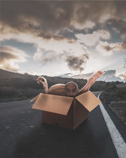 Man relaxing on road against sky