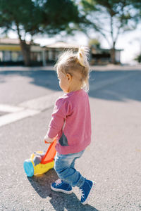 Side view of cute girl playing with push scooter on road