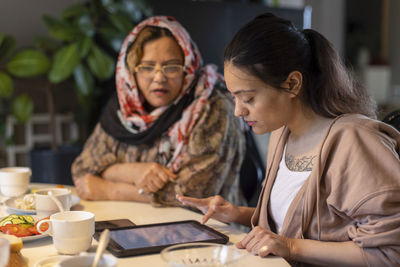 Young woman with paraplegia using tablet pc by mother sitting at dining table