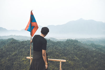 Rear view of woman standing on mountain against sky