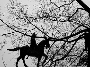 Low angle view of silhouette statue on tree against sky