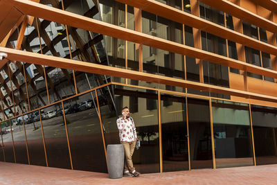 Casual wear man standing against office building while using mobile