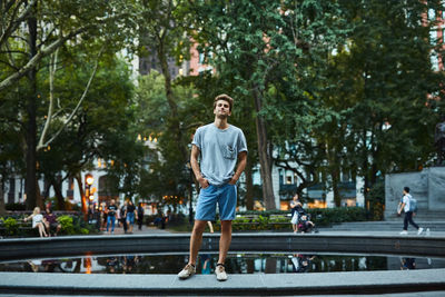 Young man standing by pond in city