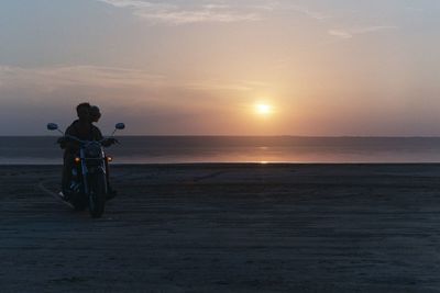 People riding on beach against sky during sunset